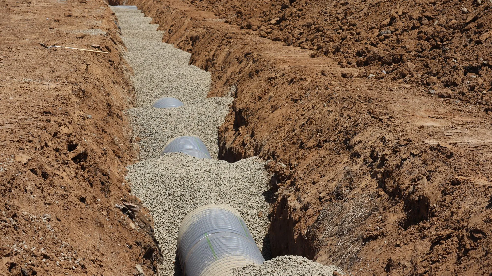 Pipe being laid in an open trench, the kind of ground work a geothermal loop takes