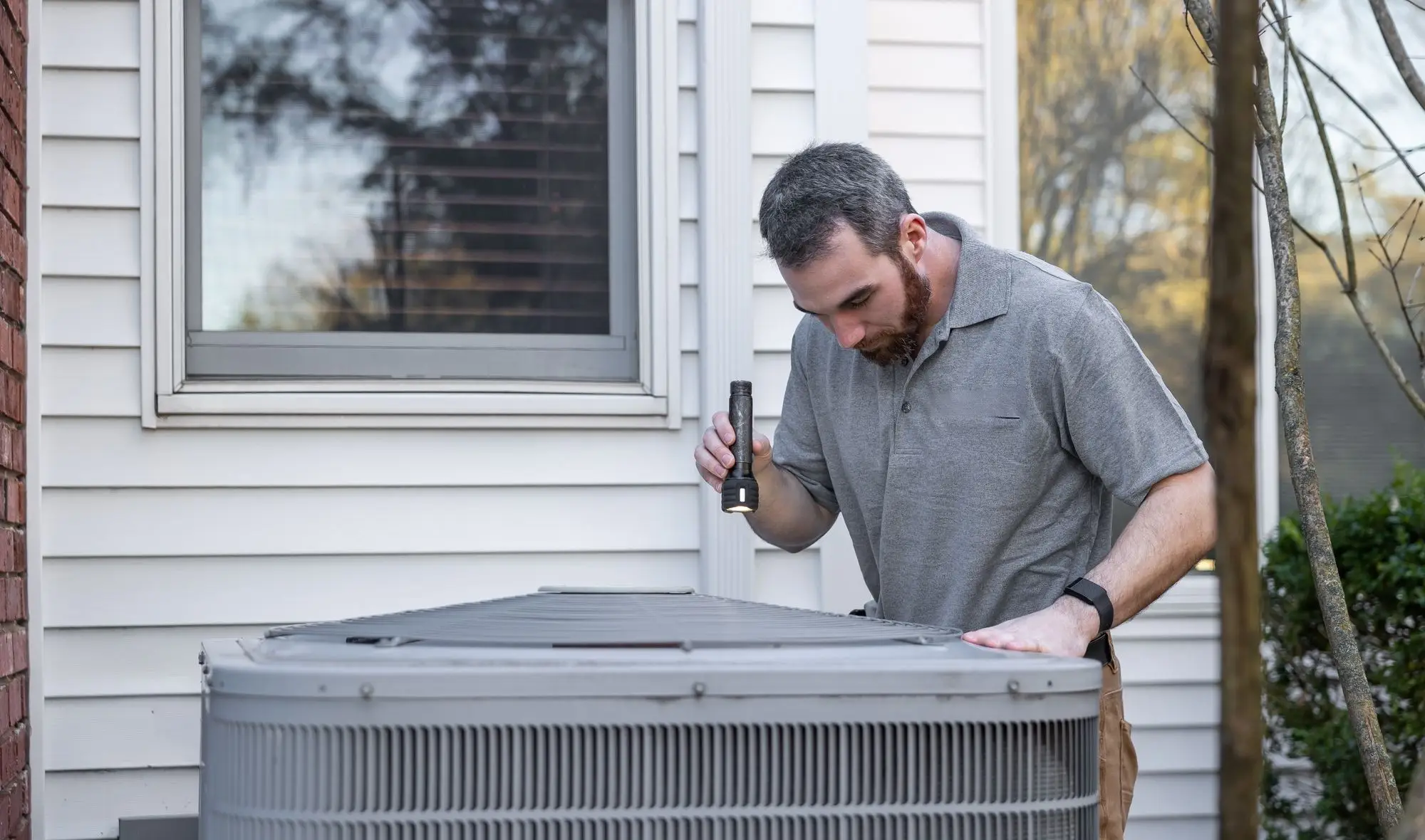 A technician inspecting an outdoor air conditioning unit with a flashlight