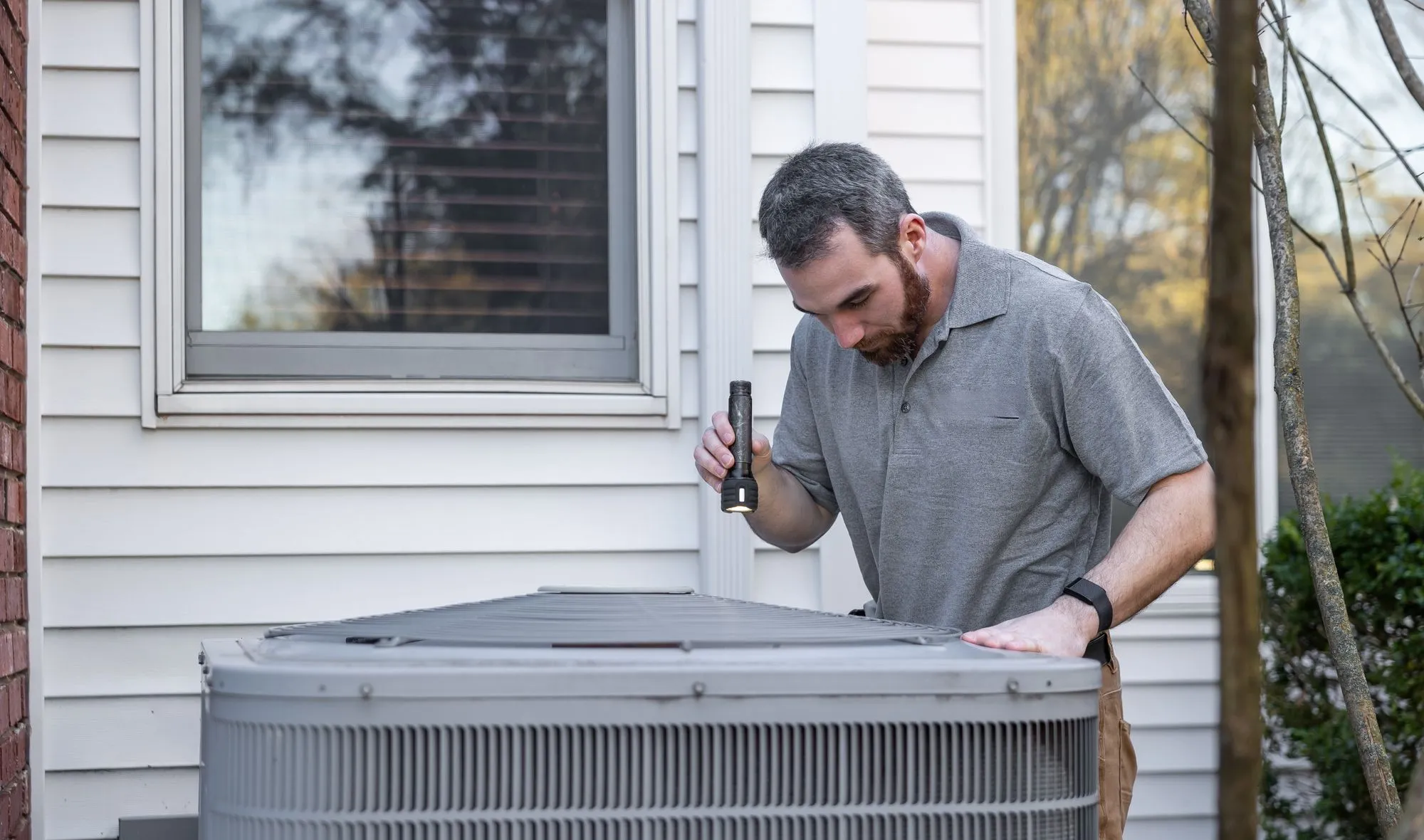 A technician inspecting an outdoor air conditioning unit with a flashlight